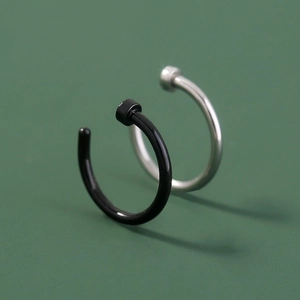 Macro shot of minimalist black and silver U-shaped stainless steel nose rings on green background