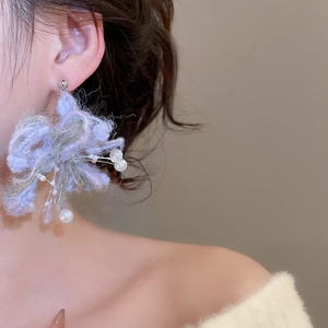Close-up of handmade purple and green knit flower earrings with white pearls on model