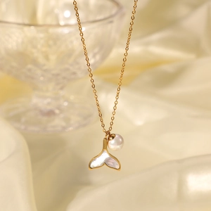 Macro shot of whale tail pendant with white shell inlay and pearl on gold chain