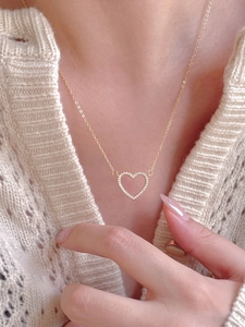 Close-up of heart pendant necklace with zircon stones worn over a cream knit sweater