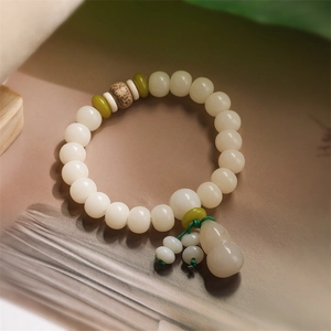 Detailed view of white Bodhi root prayer beads with green spacers and gourd charm on a book