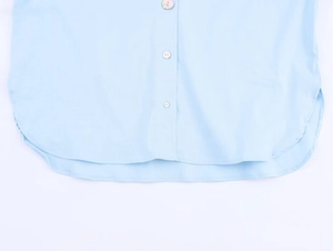 Detail view of the light blue linen shirt featuring a curved hem and buttoned placket texture