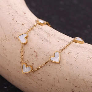 Detail of 18K gold plated bracelet featuring white shell heart charms on stone background