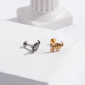 Detail of G23 titanium labret studs featuring scorpion designs in silver and gold finishes