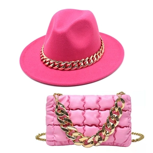 Close-up of vibrant pink fedora hat and quilted handbag with chunky gold chain accessories