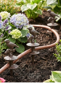Detail of vintage cast iron bird garden hose guide stakes protecting garden plants
