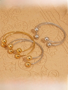 Close-up of gold and silver minimalist bangles with double ball ends on textured stone