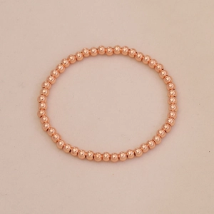 Detail of rose gold beaded bracelet featuring polished metallic spherical beads on beige