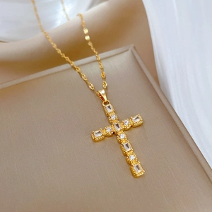Close-up of golden titanium cross necklace with inlaid cubic zirconia on a beige tray