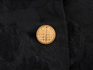 Close-up of golden textured metal button on luxury black jacquard trench coat fabric