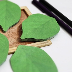 Creative green leaf-shaped sticky notes with realistic vein textures on wooden base