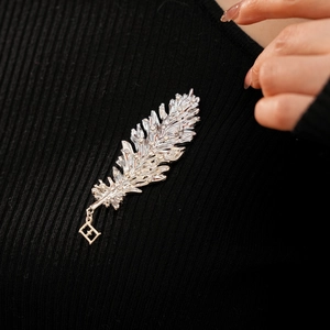 Close-up of a silver feather brooch with white crystals on a black knit garment