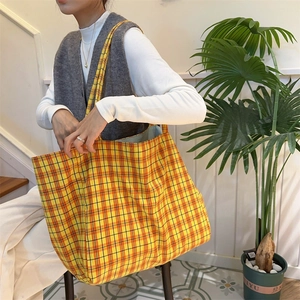 Detail view of yellow and orange plaid canvas tote bag worn by a model in lifestyle setting