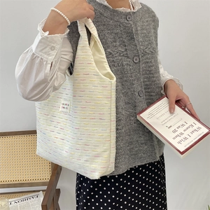 Detail view of the colorful tweed fabric texture and side brand tag on the ivory tote bag