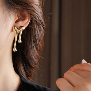 Close-up of elegant gold liquid heart earrings with a high-shine metallic finish on a model
