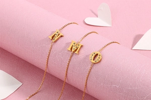 Detail of gold letter pendants M, N, O with pavé cubic zirconia on pink background