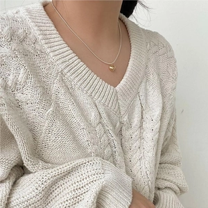 Detail of a 3D gold heart pendant on a silver snake chain worn over a white sweater