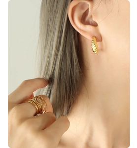 Nahaufnahme eines Models mit goldenen gedrehten C-Ohrringen und einem mehrlagigen Ring