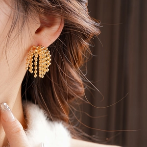Close-up of elegant gold beaded tassel earrings worn by a model in soft lighting