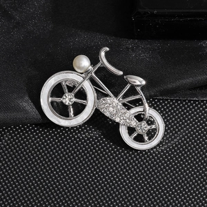 Broche vélo argentée avec cristaux brillants et perle blanche sur tissu texturé noir
