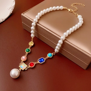 Detailed close-up of a pearl and colorful gemstone necklace on a gold jewelry box