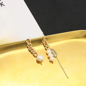 Detailed macro view of asymmetric gold plated earrings with white pearls on a tray