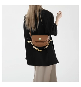 Detail of brown leather saddle bag with gold clasp and silk scarf wrapped on metal chain