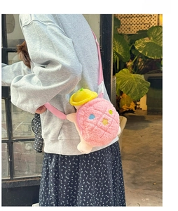 Girl wearing a pink plush turtle crossbody bag with colorful embroidery and a hat