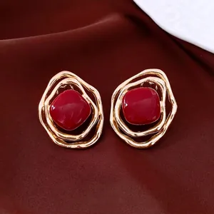 Retro gold irregular hollow earrings with red enamel center on red silk fabric background