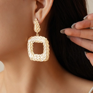 Macro detail of golden geometric square earrings with vintage wheat texture on earlobes