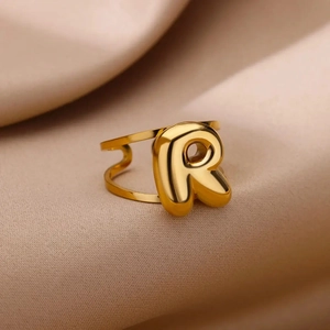 Macro detail of golden letter R ring with double-track band on beige velvet