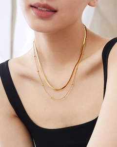 Detailed view of layered gold snake chain and beaded necklace on a model's neck