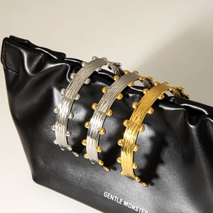 Textured gold and silver open bangles with metallic bead accents on a black bag