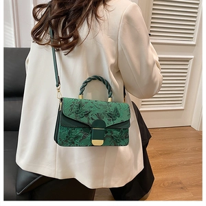 Green embroidered floral crossbody bag with woven handle shown on white blazer model
