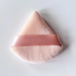 Close-up of a pink triangular velvet makeup powder puff with a satin finger strap