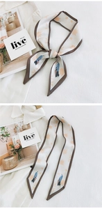 Detail of slim beige silk scarf with maple leaf print and character motif tied as a bow