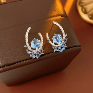 Detail view of U-shaped silver earring featuring a hexagonal light blue gemstone and zircon crystals