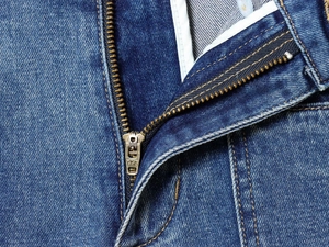 Detailed close-up of high-waisted blue denim jeans featuring a YKK zipper and yellow stitching
