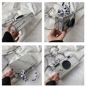 Detailed view of silver camera-shaped crossbody bag with polka dot ribbon handle and chain