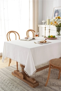 Detailed view of solid white washed cotton tablecloth featuring decorative white pom pom fringe