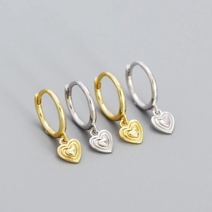 Macro detail of gold and silver heart hoop earrings showing metallic texture and finish