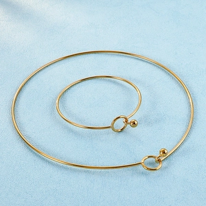 Minimalist gold-plated collar and bangle set featuring spherical clasps on blue fabric