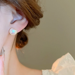 Close-up of model wearing iridescent mermaid pearl stud earrings with gold plating