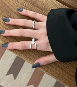 Detail of 925 sterling silver stirrup and plain rings on fingers over wood surface