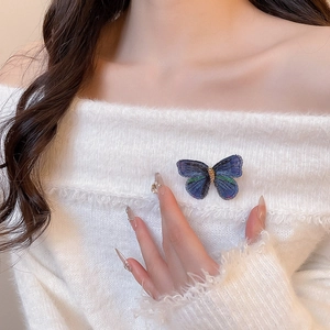 Detail of embroidered blue butterfly brooch pinned on a white knit sweater