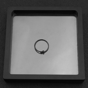 Detail of a minimalist black stainless steel geometric ring with bead on display stand