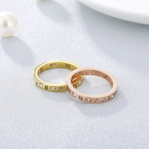 Close-up of gold and rose gold Roman numeral rings with sparkling crystals on pearl surface