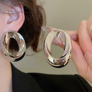Macro detail of large silver oval hoop earrings with a polished metallic finish and twist