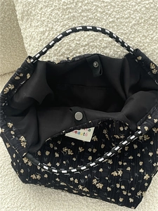 Detail view of floral canvas tote bag with black rope handles and interior metal snap button