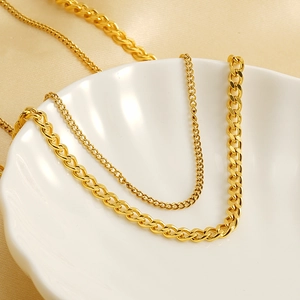 Golden stainless steel Cuban link necklaces in varying thicknesses on a ceramic bowl
